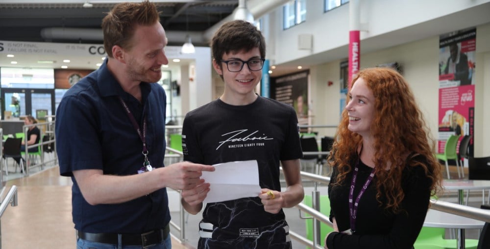 Two students smiling with a teacher about their grades.